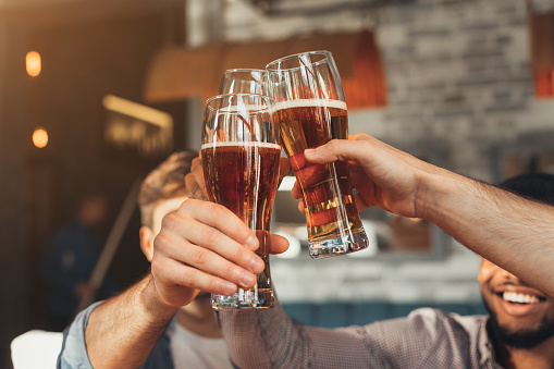 Male friends clinking beer glasses in bar, closeup
