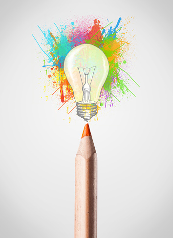 Colored pencil close-up with colored paint splashes and lightbulb concept