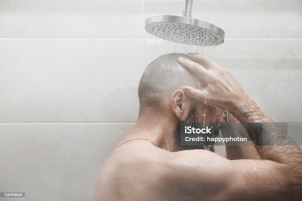 Un uomo si lava sotto la doccia. Vista laterale. - Foto stock royalty-free di Doccia