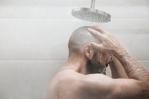 A man washes in the shower. Side view