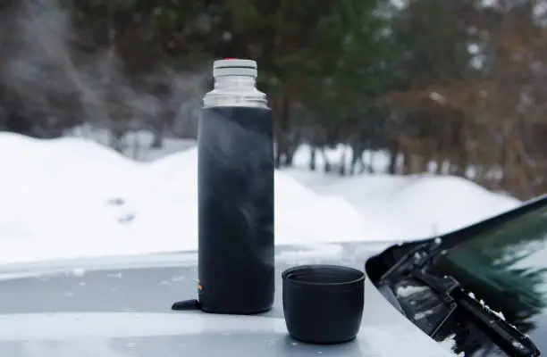 Photo of Winter picnic tea on the hood of the machine against the backdrop of the forest