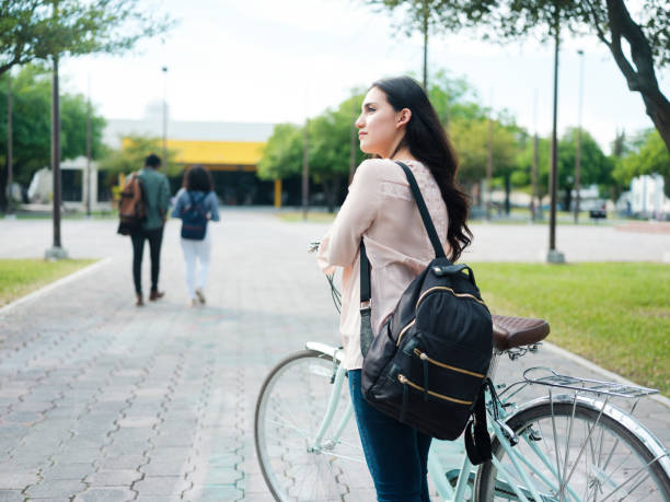 A beautiful female college student on her way to school carrying a backpack and holding a bike.