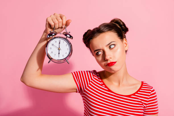 close-up portrait of her she nice cute charming attractive glamorous sad teen girl wearing striped t-shirt holding in hand showing clock boring hour isolated over pink pastel background - waiting women clock boredom imagens e fotografias de stock