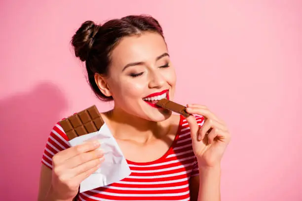 Photo of Close-up portrait of nice cute charming attractive winsome lovely glamorous fascinating feminine girl in striped t-shirt biting tasting eating desirable favorite dessert isolated over pink background