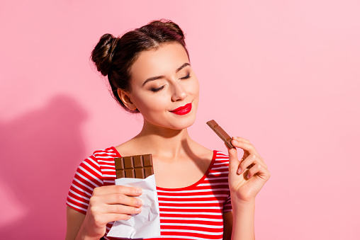 Close-up portrait of her she nice cute charming attractive winsome peaceful calm girl in striped t-shirt biting tasting desirable dessert isolated over pink pastel background.