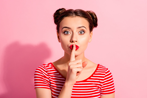 Close up photo beautiful she her lady pretty buns bright pomade lipstick arm hand finger lips asking not talk tell speak fellow friend wear casual striped red white t-shirt isolated pink background.