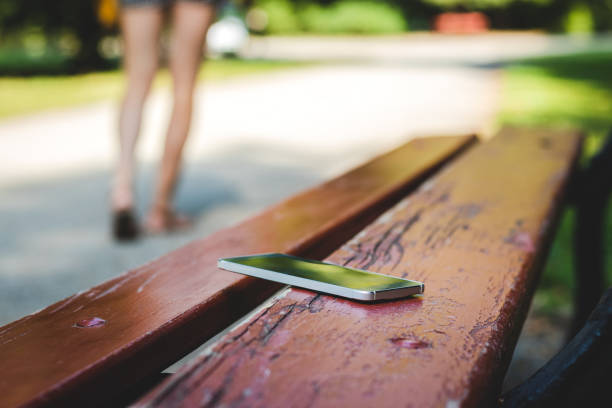 Lost smart phone on bench in public park. Woman leaving from bench where she forget her smart phone. lost stock pictures, royalty-free photos & images