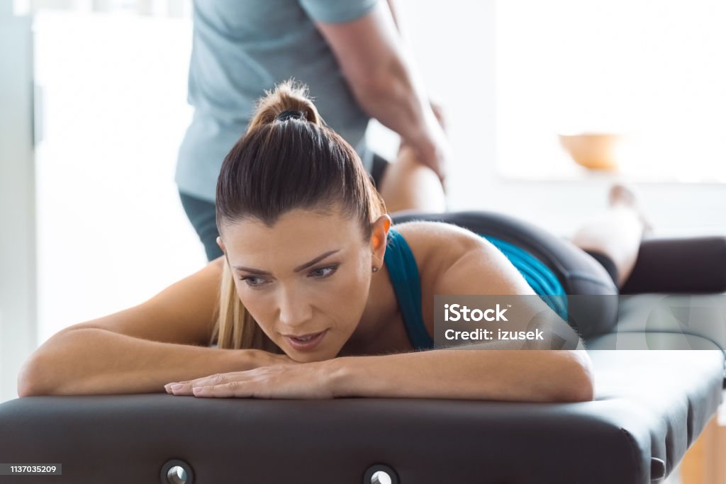 Physiotherapist massaging woman's leg Physical therapist giving leg massage to young woman. Close up of woman’s face. Adult Stock Photo