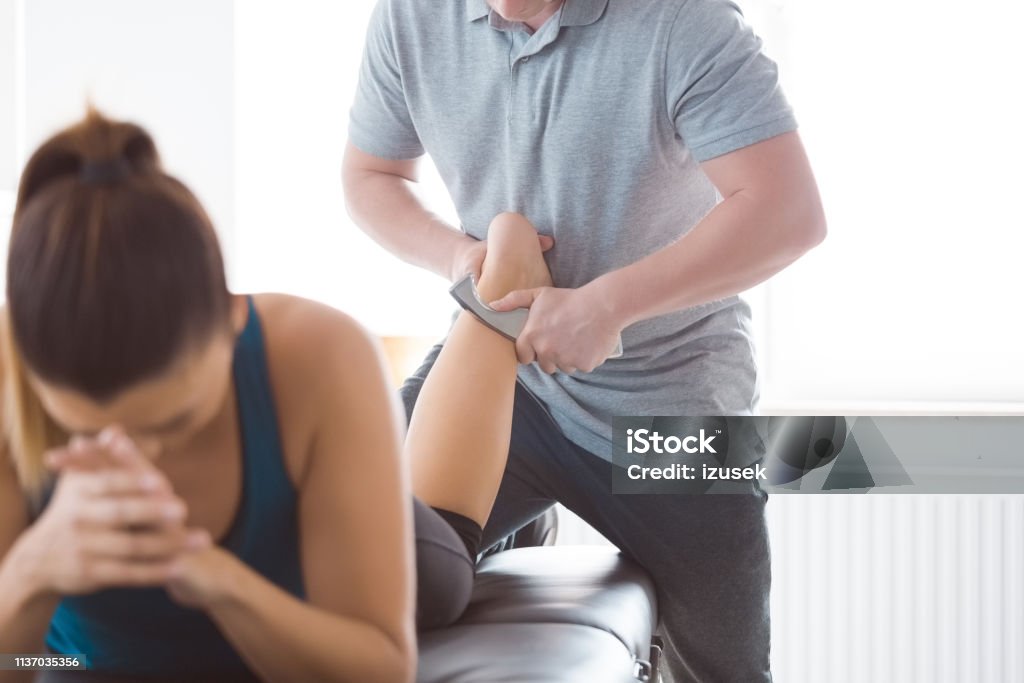 Physiotherapist massaging woman's leg using tools Physical therapist giving leg massage to young woman using tools. Focus of hands, unrecognizable people. Achilles Tendon Stock Photo