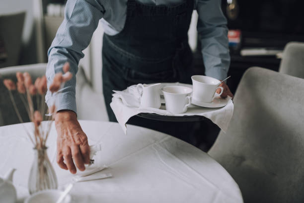 istock Waiter in apron holding tray with cups of coffee and placing sugar on table 1137035607