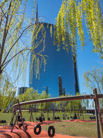View of the Unicredit Tower seen from Biblioteca degli alberi, park located between Piazza Gae Aulenti and the Isola district. 03/18/2019. Milan. Italy. People resting lying on a swing. Lunch break