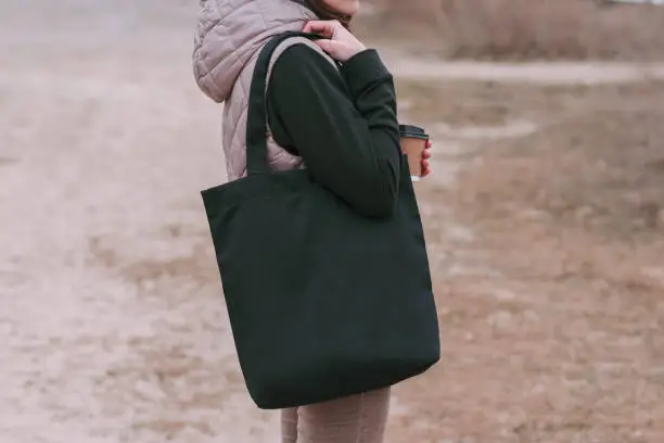 Photo of Young woman with black cotton bag and paper coffee cup in her hands. Mock up for design.