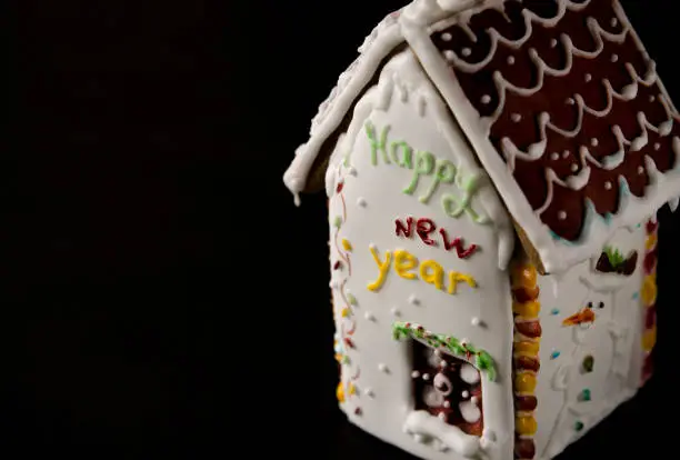 On a black background is a white gingerbread house with a brown roof, a window and the inscription happy New Year on a white wall