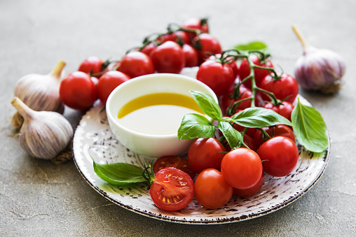 Plate with cherry tomatoes, olive oil and basil on a stone background