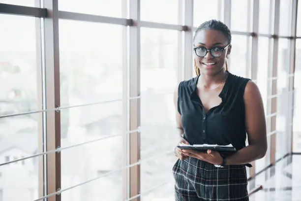 A thoughtful African American business woman wearing glasses holding documents.