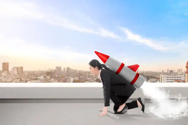 Photo of Excited asian business woman on the rooftop with rocket ready to fly