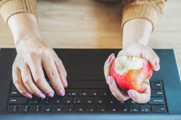 Woman hand working on computer and eating apple at desk