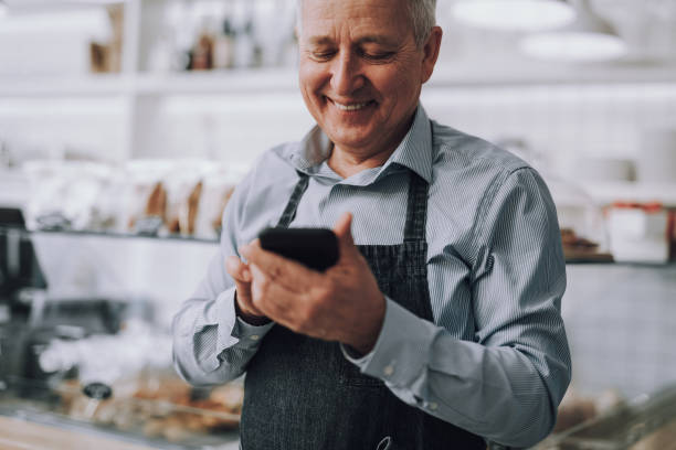 istock Joyful senior man in apron using modern smartphone 1137040811