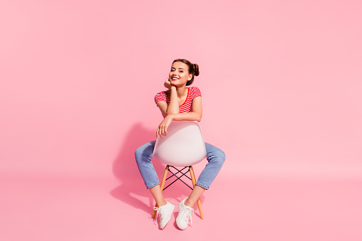 Nice-looking attractive glamorous magnificent lovely shine cheerful cheery girl wearing striped tshirt jeans sitting on chair having free time isolated over pink pastel background.