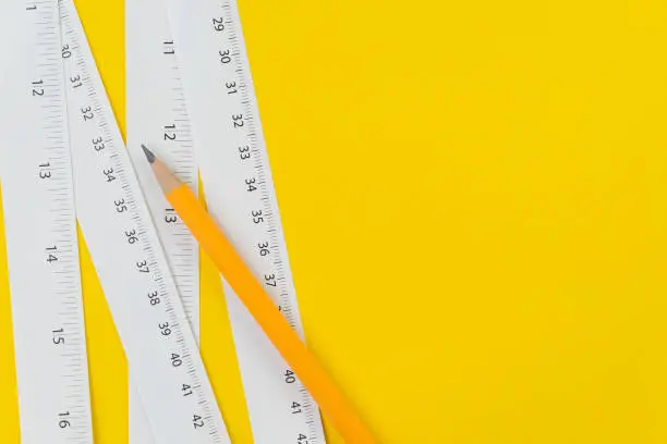 Yellow pencil and white measuring tapes with centimetre and inches on vivid yellow background, length, long or maker instrument and tools concept.