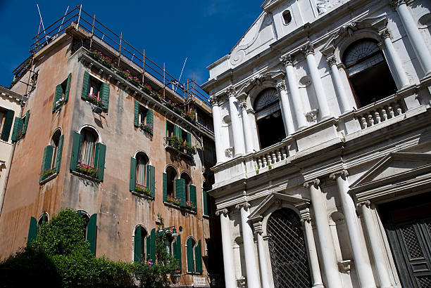 Brightly colored Venetian building facade surrounded by lush flora, showcasing intricate architectural elements and arched windows.