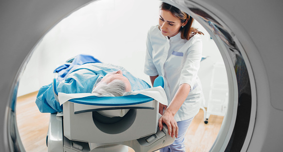 Wide angle view of a diagnostic imaging facility with MRI scanner being operated by male doctor and female patient laying on scanner bed
