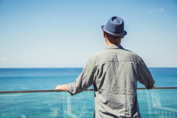 Young man is standing on a balcony and admiring the seaside view