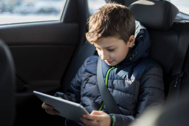 istock Boy sitting in a car and reading his ebook 1137060394
