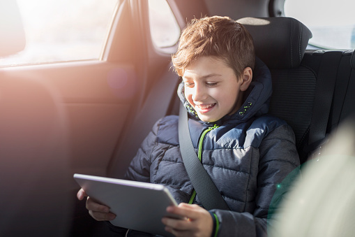Teenage boy using digital tablet in the back seat of car.  Safety of transportation of children