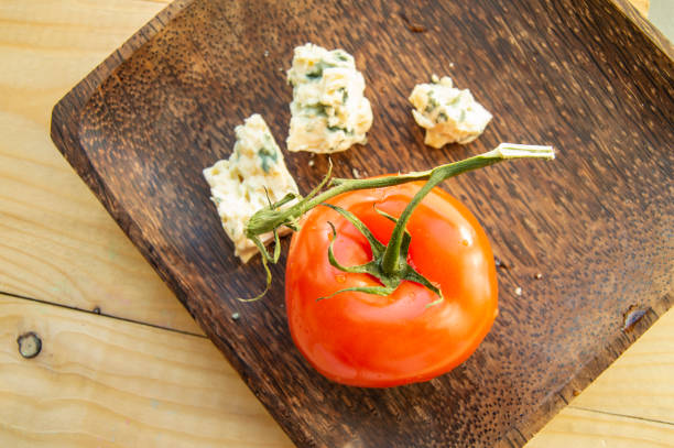 Wooden plate with tomato and cheese with mold. Flat lay top view