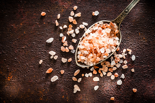 Top view of a vintage metal spoon with Himalayan salt shot on abstract brown rustic table. Himalayan salt crystals are scattered on the table. Useful copy space available for text and/or logo. Predominant colors are brown and pink. Low key DSRL studio photo taken with Canon EOS 5D Mk II and Canon EF 100mm f/2.8L Macro IS USM.