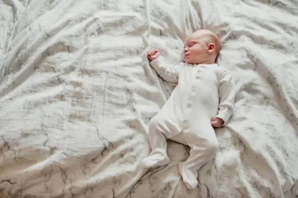 Sleeping baby boy lying on a bed looking comfortable in his bodysuit.