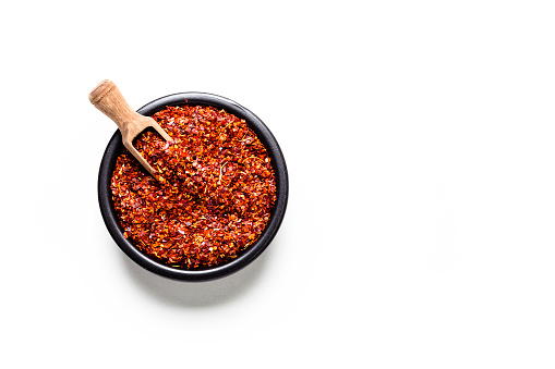 Spices: Top view of a black bowl filled with red chili pepper flakes isolated on white background. Predominant colors are white and red. High key DSRL studio photo taken with Canon EOS 5D Mk II and Canon EF 100mm f/2.8L Macro IS USM.