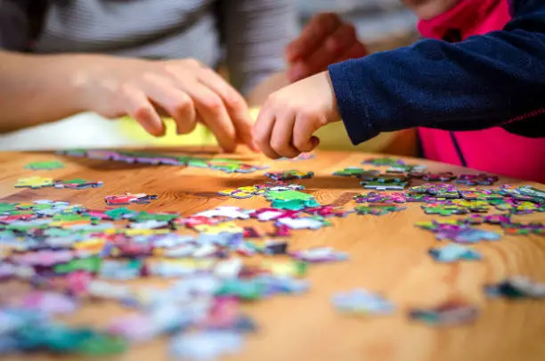 Hands of a little child and parent plying jigsaw puzzle game on a wooden table