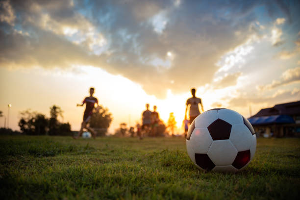 An action sport picture of a group of kids playing soccer football for exercise in community rural area under the sunset. soccer football action from kids.Silhouette action sport outdoors of a group of kids having fun playing soccer football on green grass field soccer soccer ball kicking adult stock pictures, royalty-free photos & images