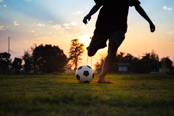 un'immagine di sport d'azione di un gruppo di bambini che giocano a calcio per l'esercizio fisico nell'area rurale della comunità sotto il tramonto. - fitness goal foto e immagini stock