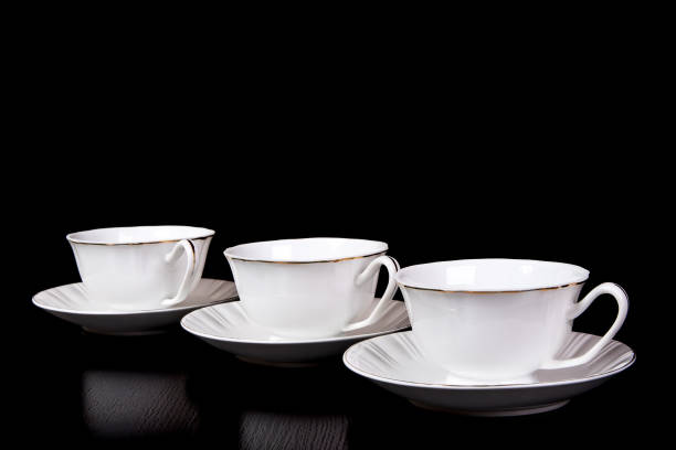drei weiße teekannen in untertassen stehen auf schwarzem hintergrund auf dem tisch - hot chocolate hot drink high section color image stock-fotos und bilder