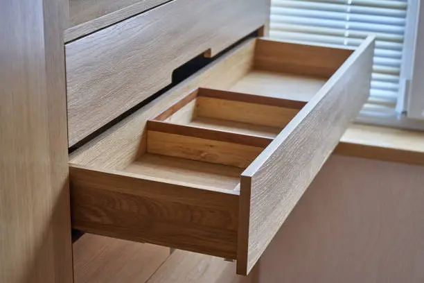 Interior wooden cupboard with empty shelves and opened drawer in daylight. Modern furniture