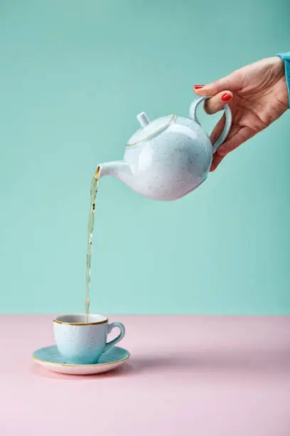 Tea pot pouring tea in a cup on blue backdrop