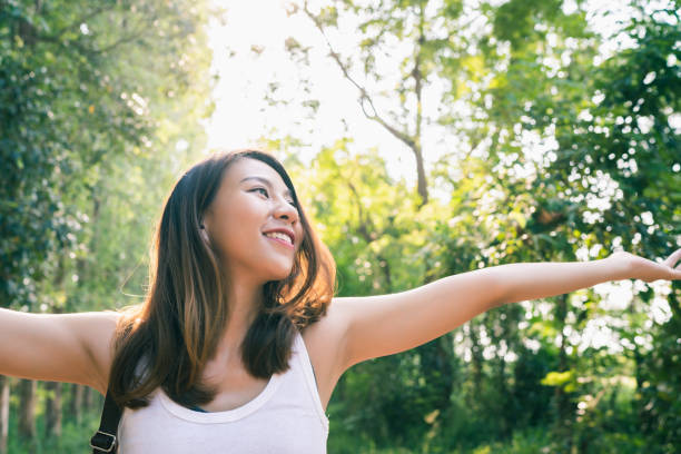 happy young asian woman traveler with backpack walking in forest. hiker asian woman with backpack walking on path in summer forest. adventure backpacker travel people concept. - tree area footpath hiking woods imagens e fotografias de stock