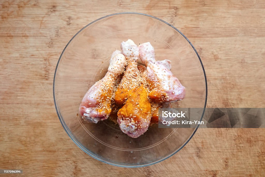 Above view of raw chicken drumstick legs with seasoning and garlic Above view of raw chicken drumstick legs with seasoning and garlic in glass bowl on wooden background, preparation for frying Chicken Meat Stock Photo