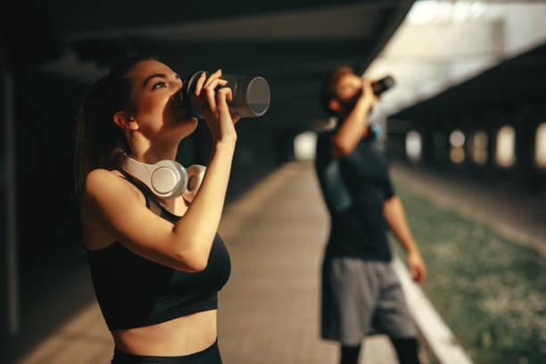 молодая женщина и мужчина пьют протеиновый коктейль после тренировки - drinking water drink men стоковые фото и изображения