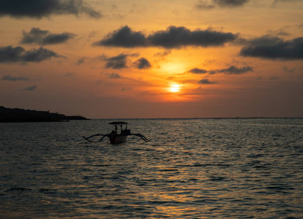 バリのボートで穏やかな海に沈む夕日 - jukung ストックフォトと画像