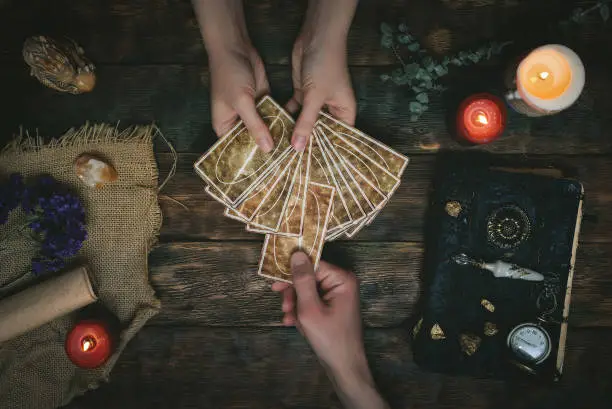 Tarot cards, magic book and fortune teller hands on a wooden table background. Future reading concept. Divination.