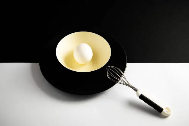 White egg on a yellow bowl resting on a black and white surface