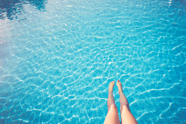Woman relaxing by blue swimming pool with stretched out legs - POV Point of view