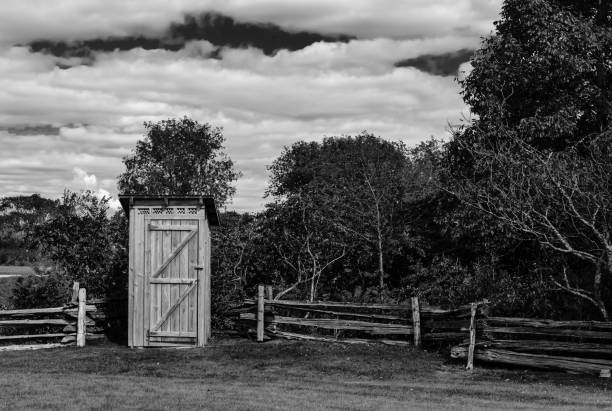 Rustic outhouse next to a split rail fence and trees in Black and white