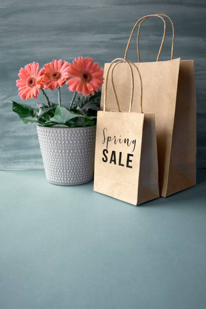 istock Coral gerbera daisy flowers and craft papper shopping bags on paper background, text 