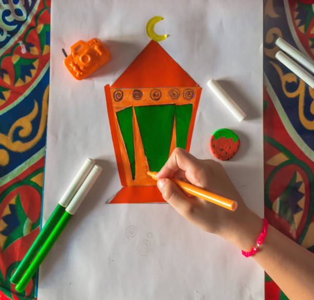 Young Muslim kid hand drawing Ramadan lantern on white paper