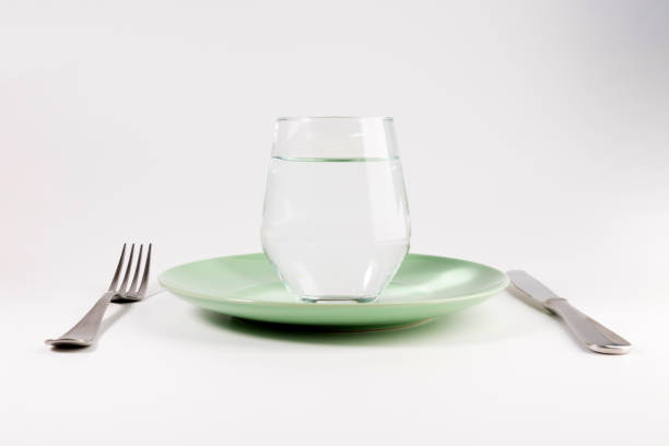 glass of water in a plate with knife and fork isolated on white background stock photo